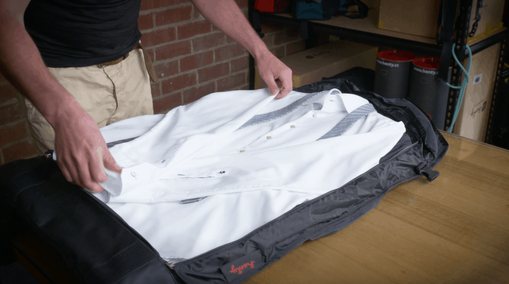 A man places a folded white business shirt and tie inside a Henty garment bag.