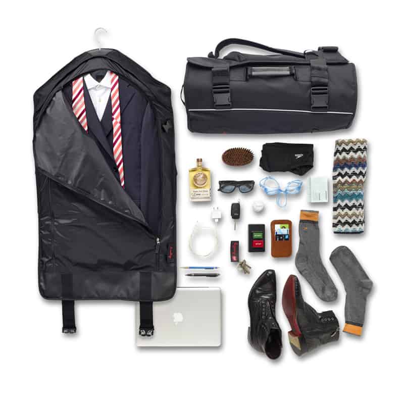 A suit inside the CoPilot backpack, surrounding by various belongings including shoes, a laptop, sunglasses, and socks.