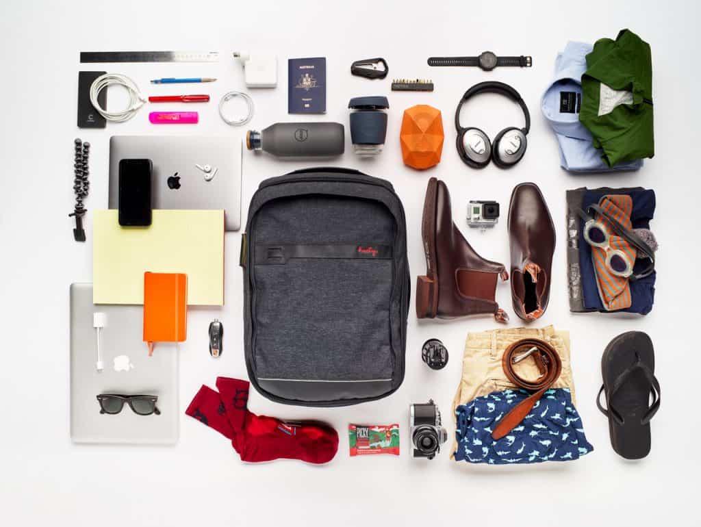 Henty Travel Brief surrounded by different travel products including headphones, shoes, clothes, underwear, passport, laptop, and more.